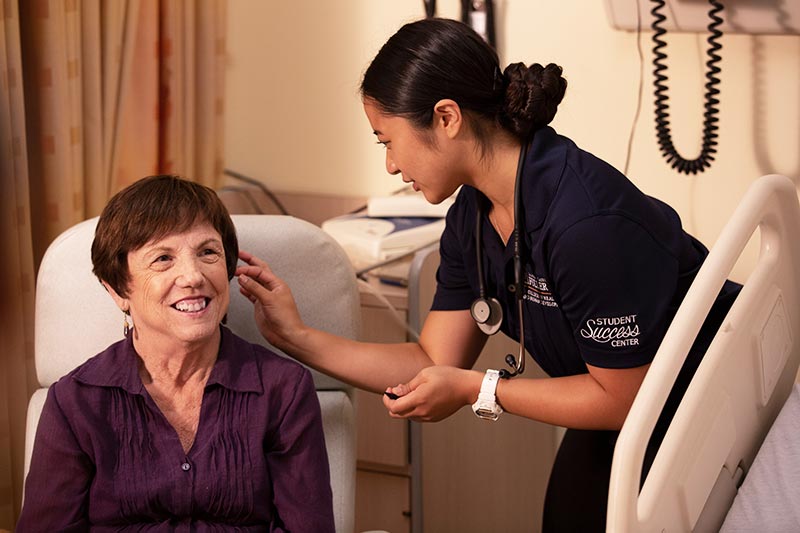 Nursing student examining ear of elderly patient